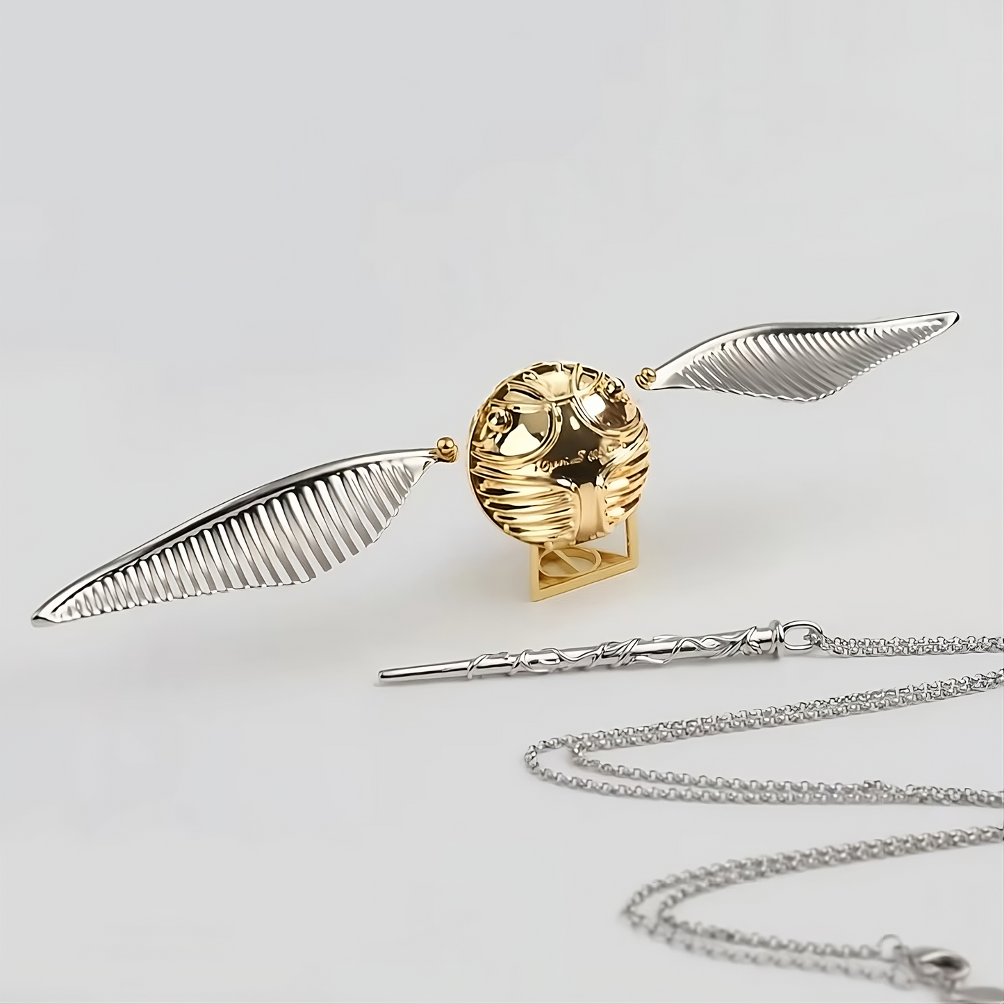 Gold and silver objects including a broomstick, golden snitch, and necklace on a light gray background