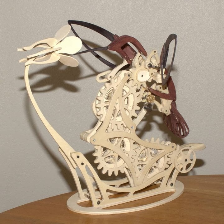 Mechanical model of a horse with gears on a wooden base against a DIY Puuzzle | Kinetic Hummingbird Sculpture - 3D Wooden Mechanical Puzzle Kit