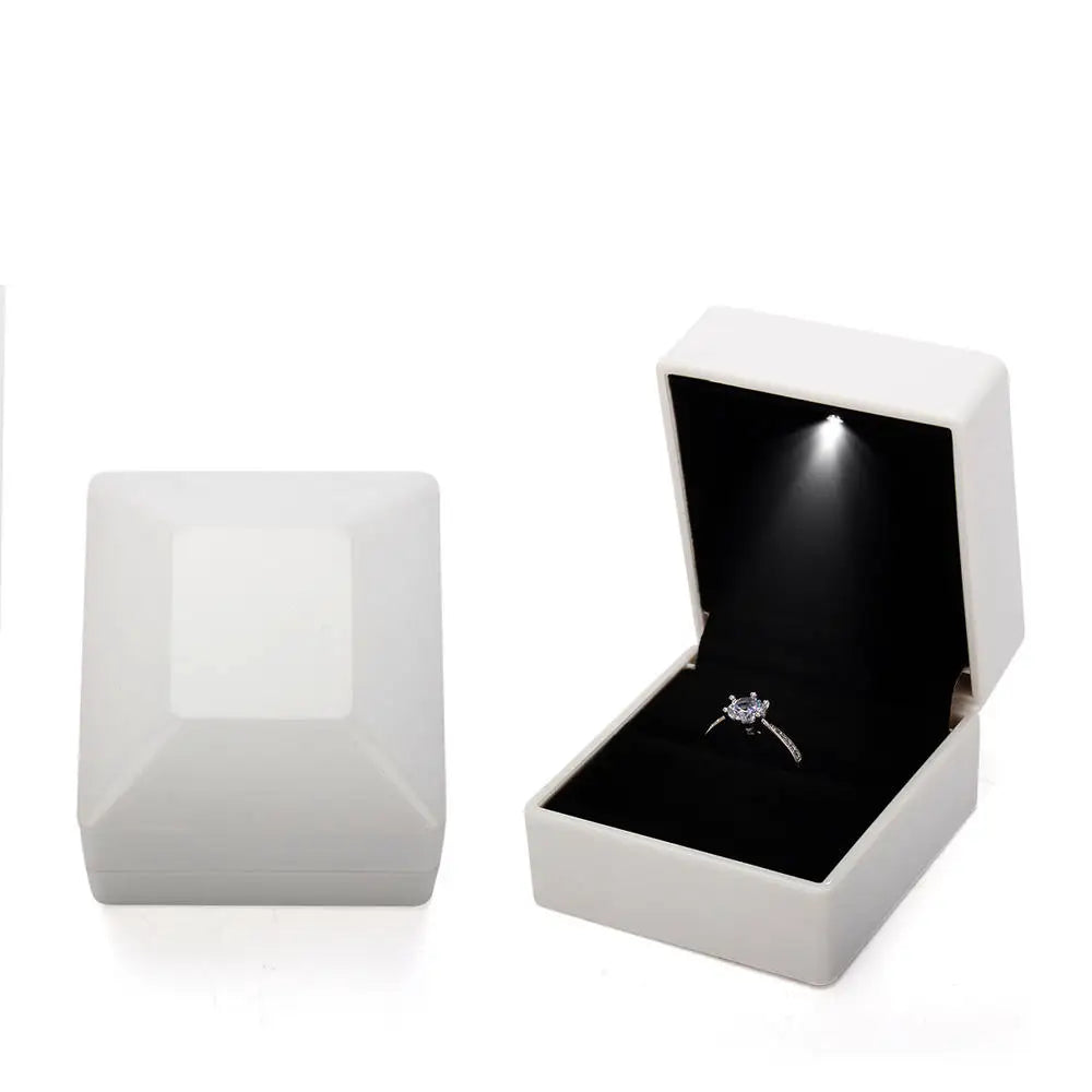 Open white jewelry box with a black interior containing a diamond ring on a LED ring box with automatic light for engagement proposals and wedding jewelry display