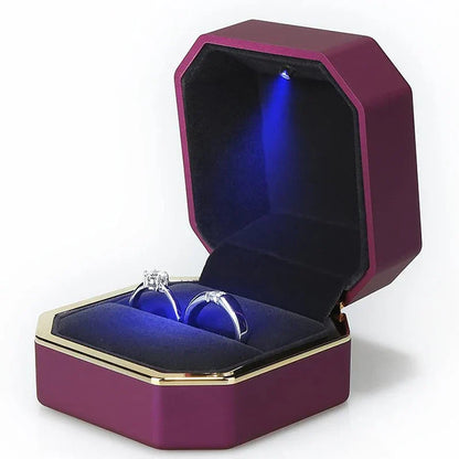 Purple jewelry box with a blue interior containing a ring, illuminated from within. LED ring box with automatic light for engagement proposals and wedding jewelry display