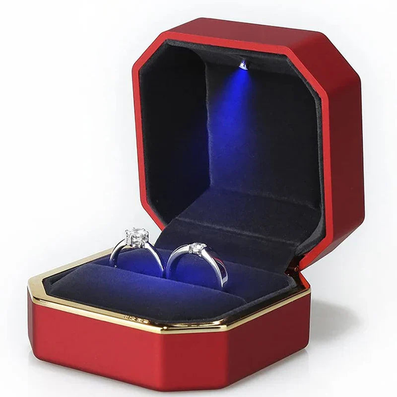 Red jewelry box with blue interior containing two silver rings LED ring box with automatic light for engagement proposals and wedding jewelry display