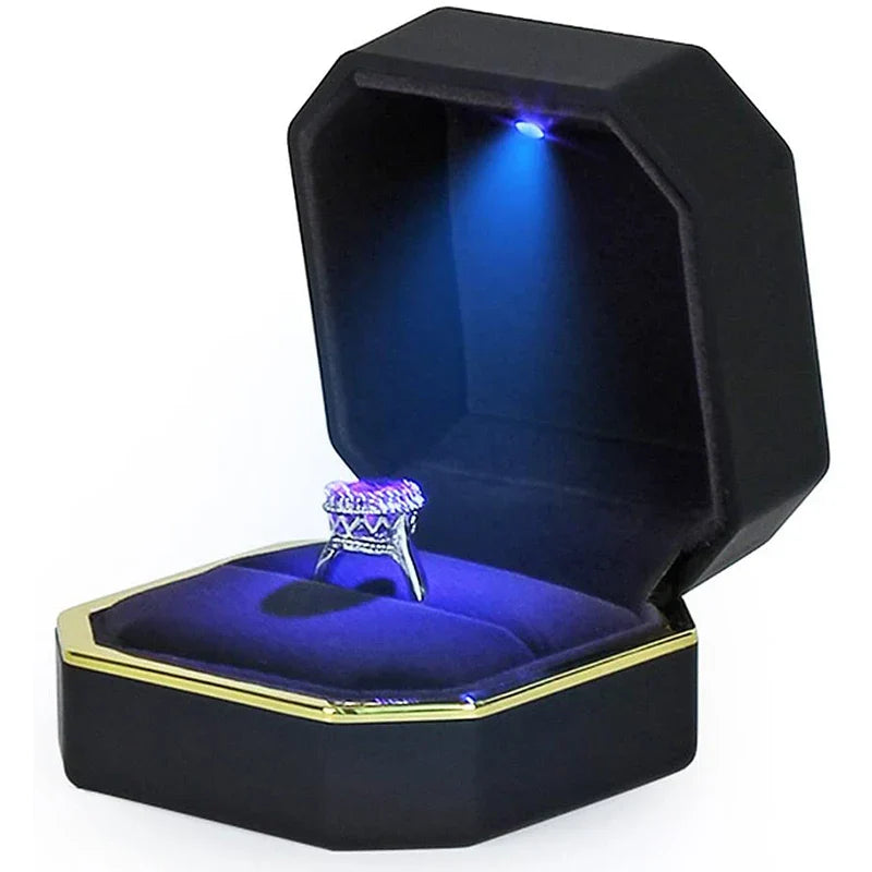 Black jewelry box with blue interior containing a ring, illuminated from below.