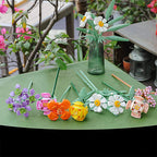 Colorful flower-shaped straws on a green surface with a blurred garden background.