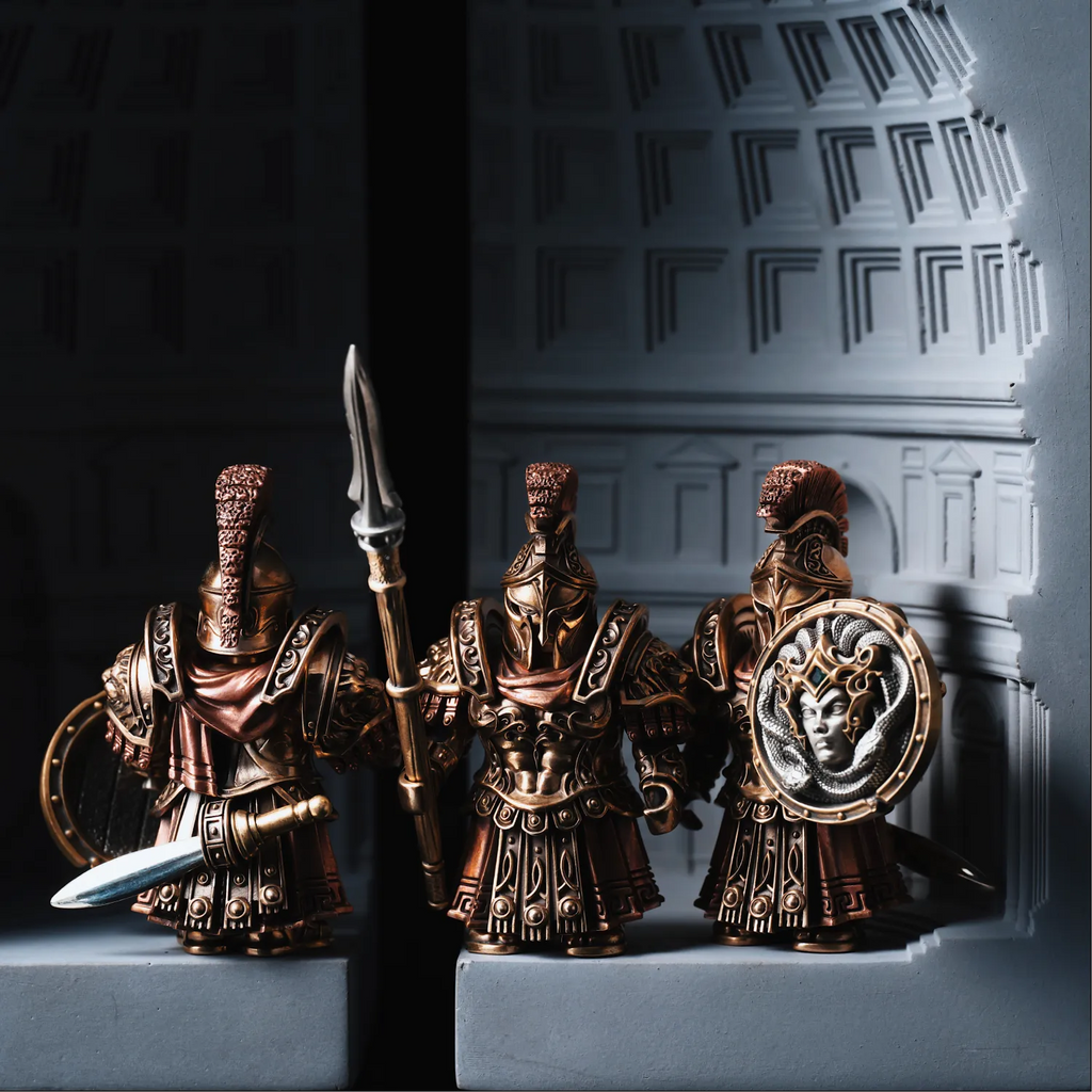 Three bronze-colored warrior figurines with armor and weapons on a textured surface.