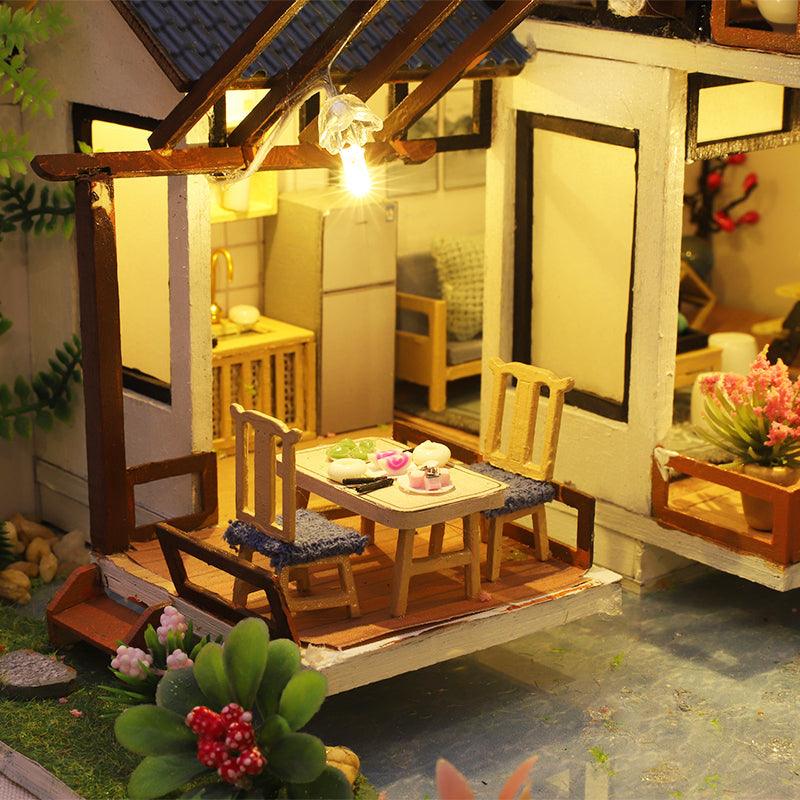 Miniature dining table and chairs beside a cozy kitchen, a music box dollhouse craft kit and display gift for makers