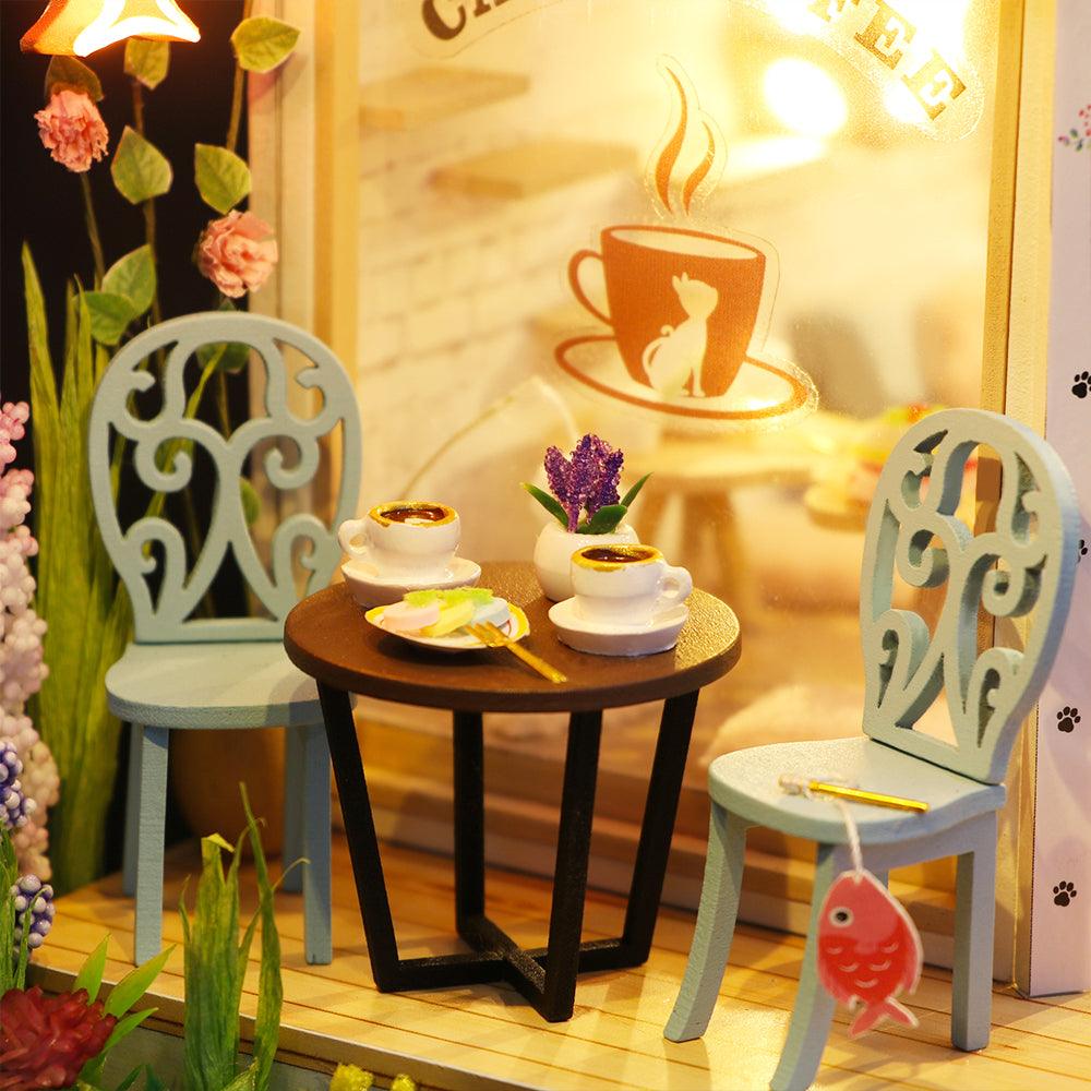 Tiny garden cafe table set with scrollwork chairs, coffee cups and blooming flowers, a cozy craft model for cat and coffee fans