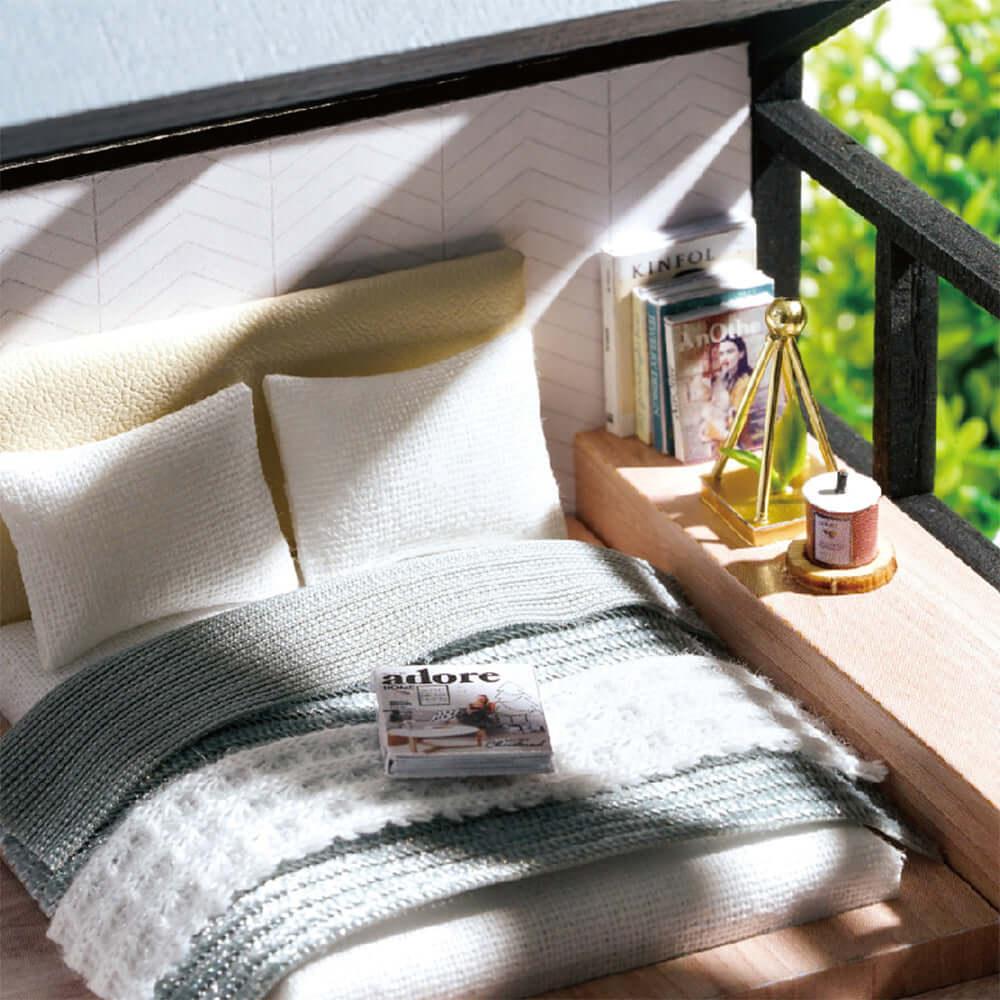 Blue toned miniature bedroom with a made bed, books and a lamp, part of a 1:24 scale DIY apartment dollhouse kit for hobbyists