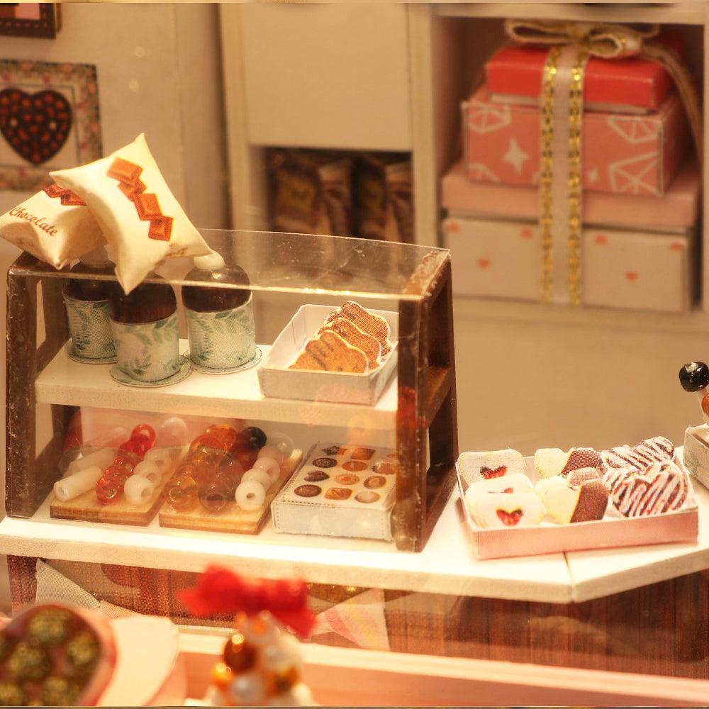Lit miniature chocolate shop display case with tiny pastries and a clear dust cover for long term desk decor