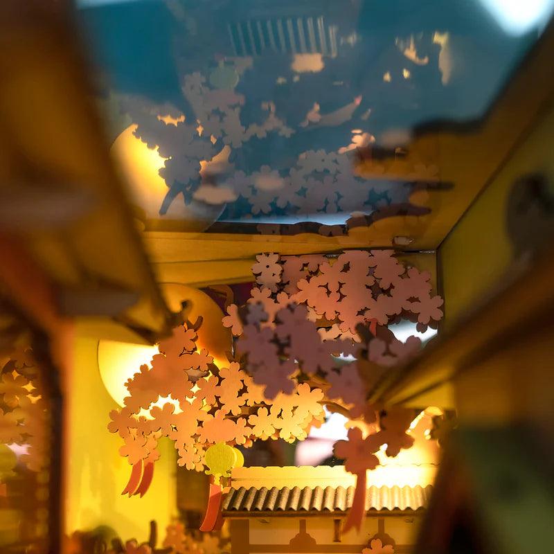 Warm LED lighting over pink cherry blossoms in a Japanese book nook, ambient sakura shelf decor for a reading nook