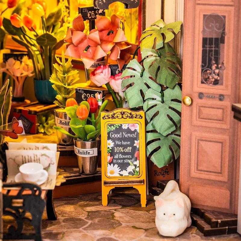 Detailed miniature flower market with potted blooms, tiny price signs, and a ceramic cat, a floral book nook for crafters