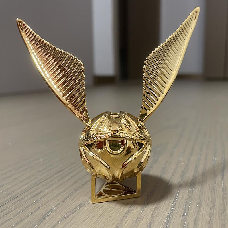 Golden Snitch display piece standing on a stand with spread wings, a Harry Potter desk decor collectible for fans RNGBX1