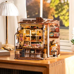 Finished chocolate shop miniature house on a desk beside a lamp, a relaxing laser-cut craft project and display gift for hobbyists