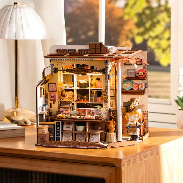 Finished chocolate shop miniature house on a desk beside a lamp, a relaxing laser-cut craft project and display gift for hobbyists