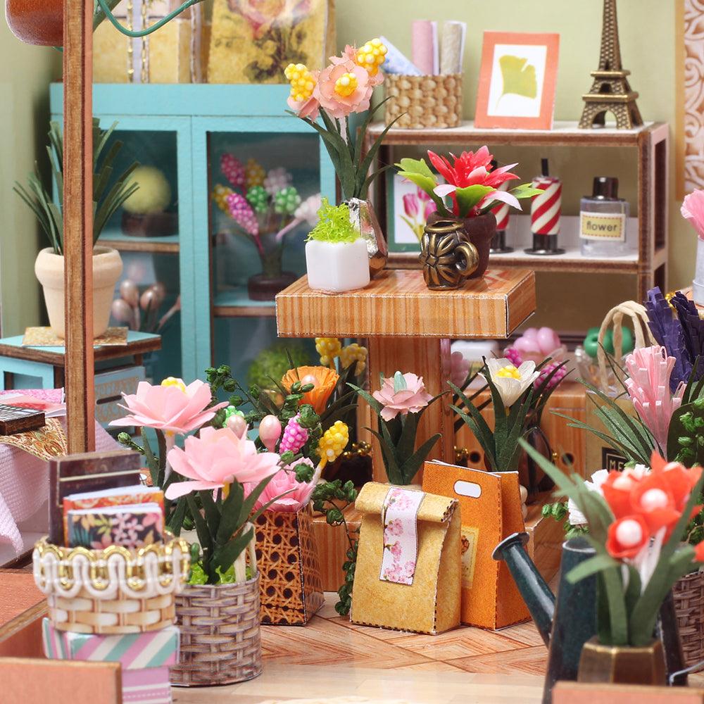 Miniature flower shop scene with potted blooms, wooden display stands, and gift bags, a 1:24 DIY dollhouse kit for adults
