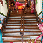 Narrow staircase descending into the street scene book nook past decorative tiles toward a colorful lit storefront