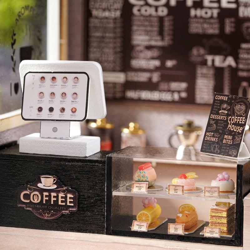 Tiny cafe counter with a register and a glass dessert case of cakes below a wall menu, a cozy craft model for coffee shop fans