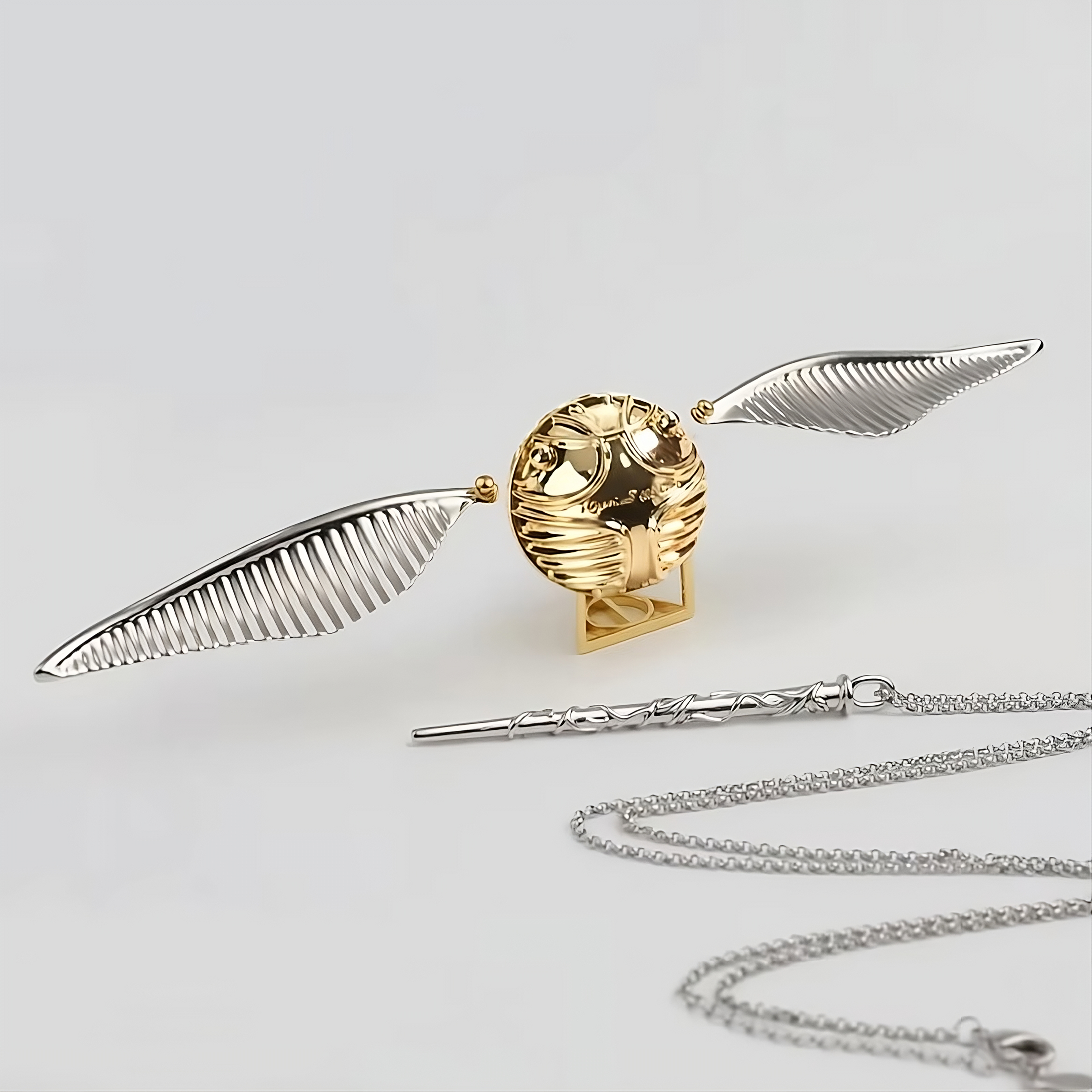 Gold and silver objects including a broomstick, golden snitch, and necklace on a light gray background