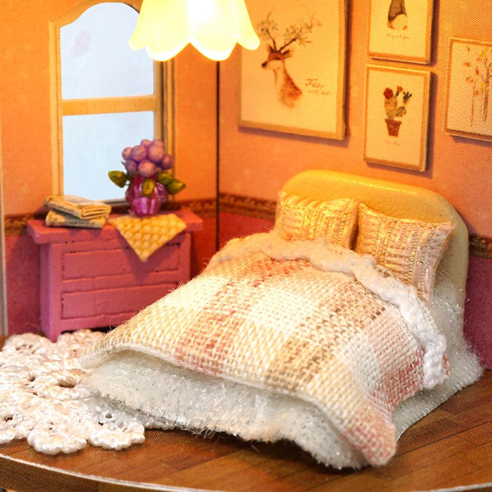 Warmly lit bedroom scene with a knit bed set and framed deer wall art in a hands on miniature dollhouse kit for crafters