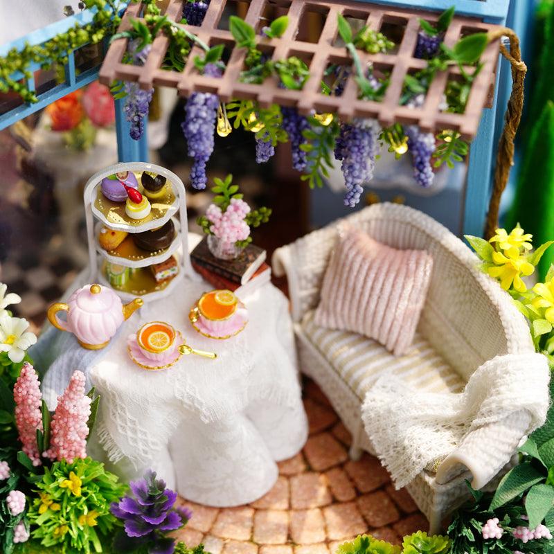 Miniature garden patio tea lounge with wicker sofa, wisteria pergola, and lace tea table, a floral room box diorama