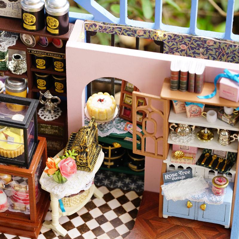 Miniature tea shop interior stocked with tea tins, a cake stand, and pantry shelves, a dollhouse kit for collectors