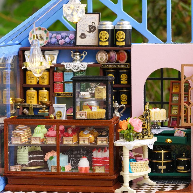 Miniature bakery counter with a glass cake cabinet, brass scale, and tea tins, a music box dollhouse gift for adults