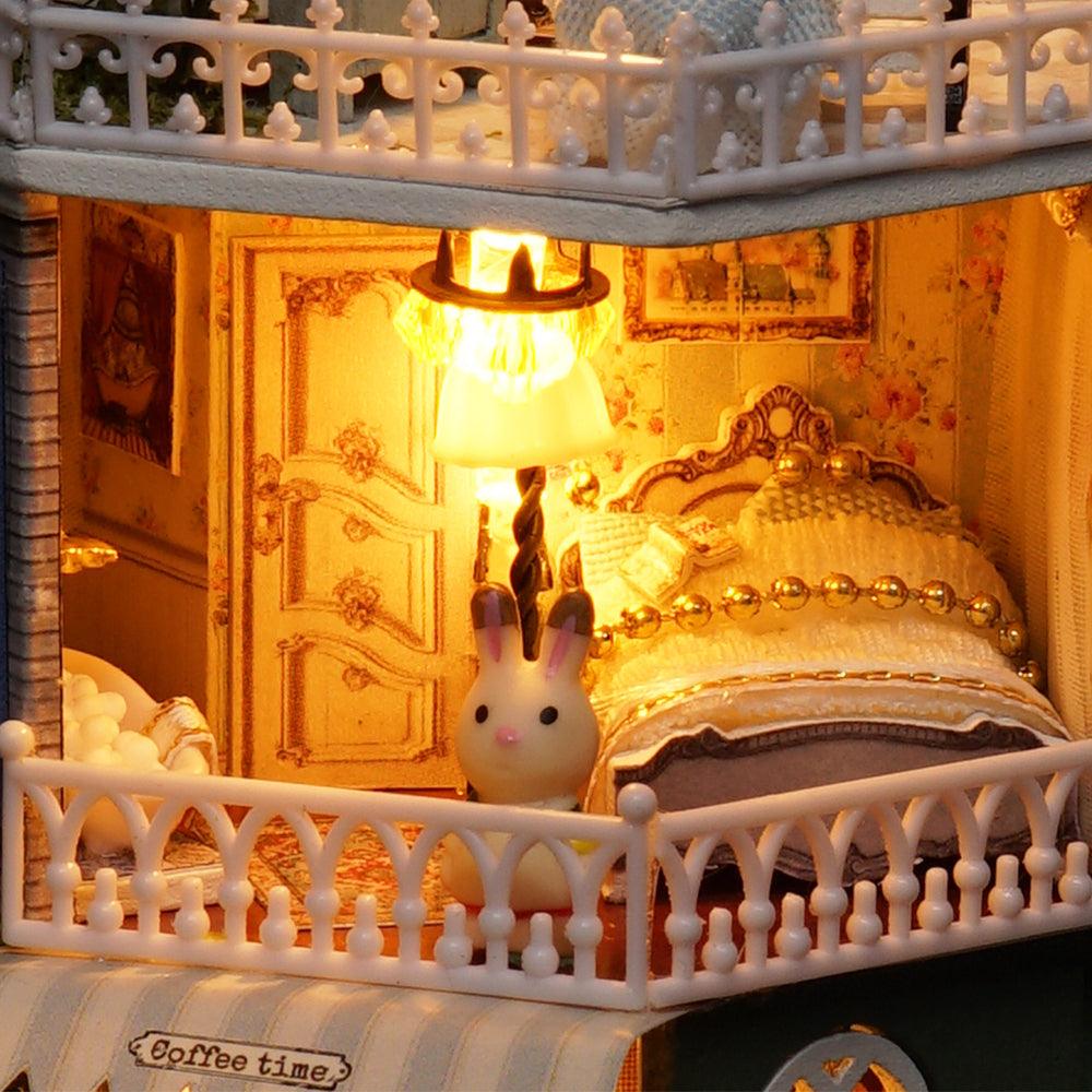 Illuminated 1:24 bedroom with an ornate bed, glowing lamp and floral walls in a handmade miniature dollhouse