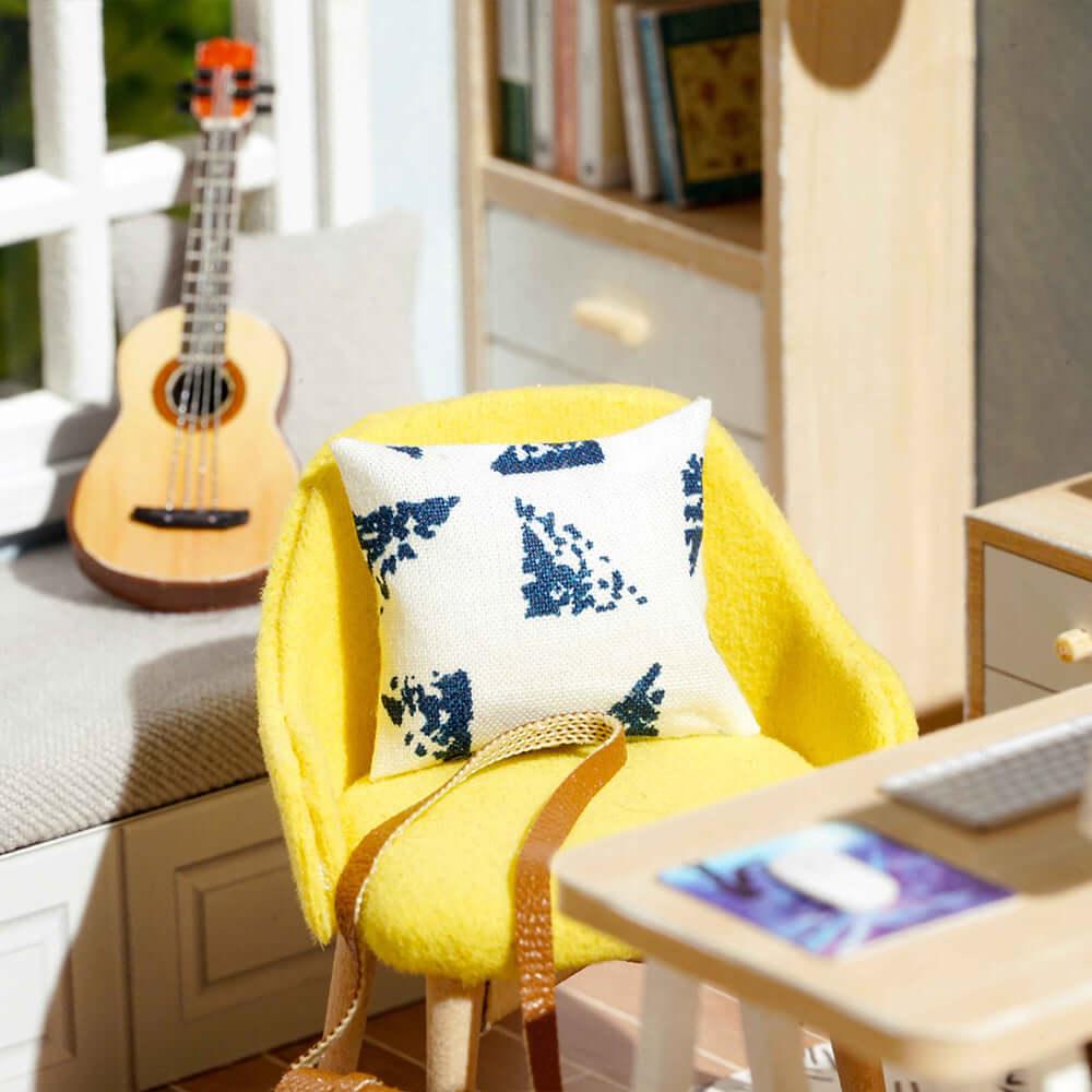 Cozy reading nook with a yellow accent chair, patterned pillow and ukulele in a sunlit miniature dollhouse kit