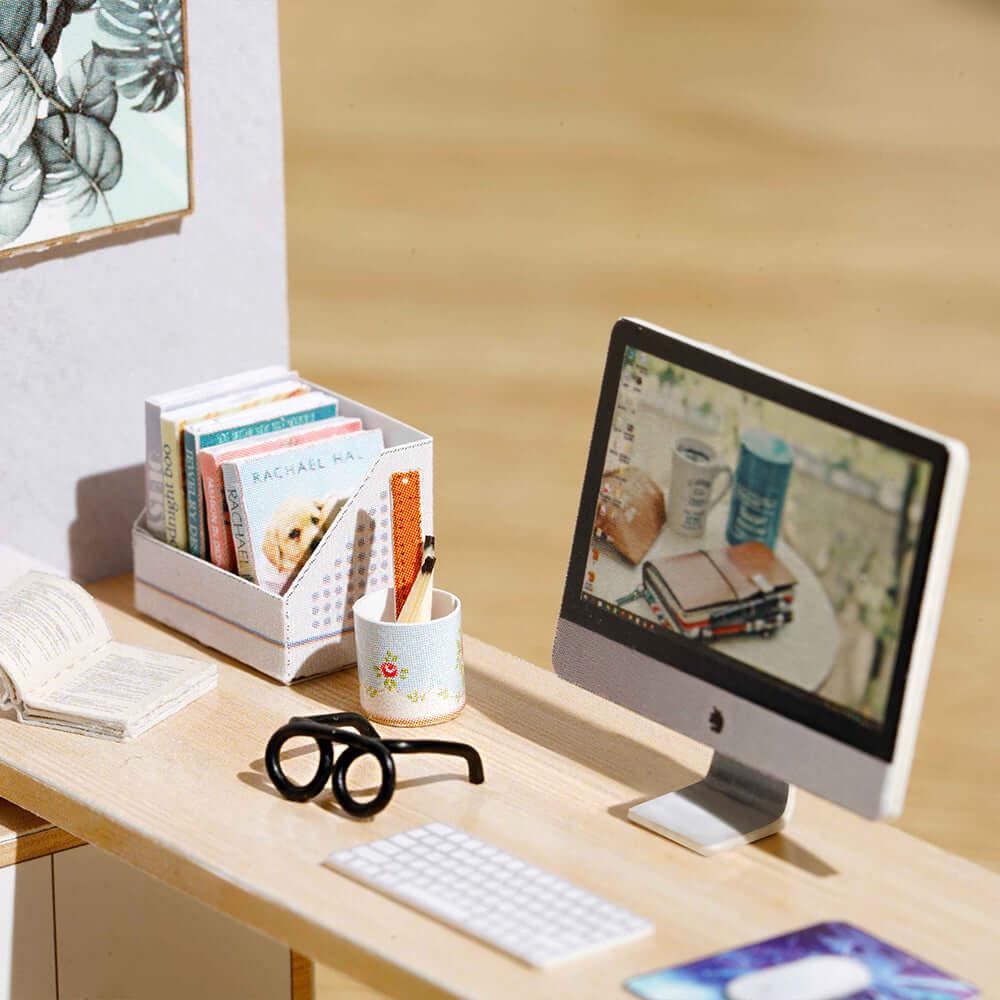 Miniature home office desk with a computer, tiny books and eyeglasses in a bright furnished 1:24 dollhouse room