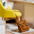 Handcrafted leather bag beside a yellow chair in a sunlit miniature dollhouse room kit, a craft gift for ages 14 up