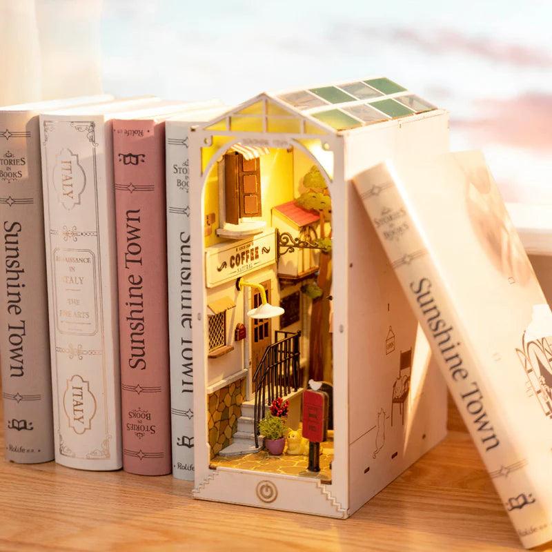 Cozy bookshop nook lit by amber light over cobblestone streets, a glowing miniature diorama for a desk or bookshelf display