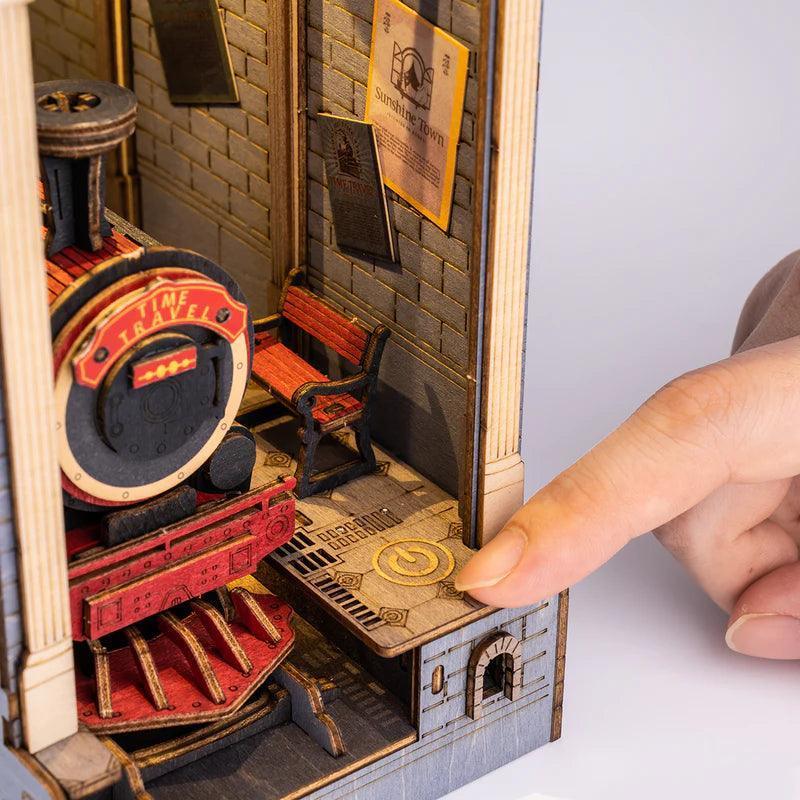 Red steam locomotive waiting at a lit station platform inside the wooden railway book nook, a model train kit for hobbyists
