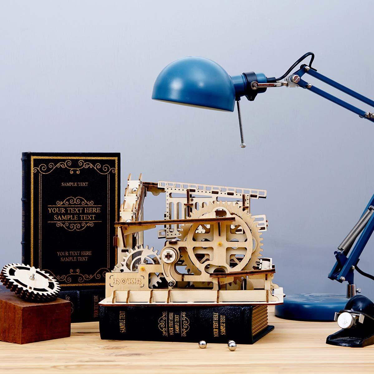 Trapdoor marble run styled as desk decor beside books, a mechanical 3D wooden puzzle and STEM gift for curious builders
