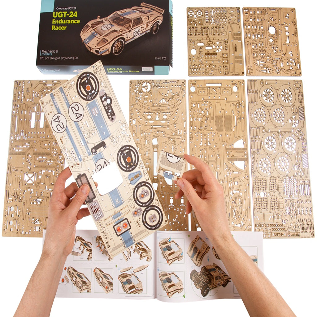 Hands assembling a laser cut wooden race car at a desk, a glue free building project and hands on gift for adult model makers