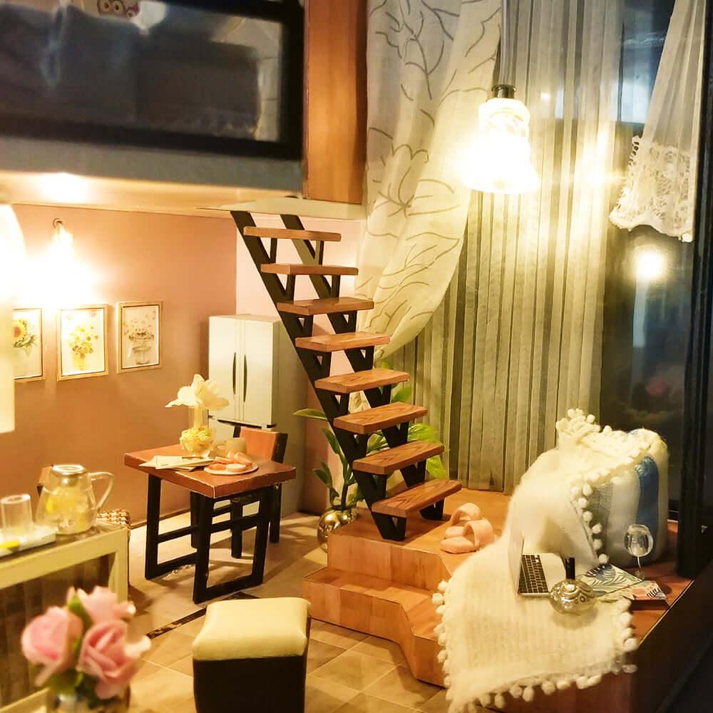 Miniature room box with a wooden staircase, dining table and warm LED lighting for a cozy handmade shelf display
