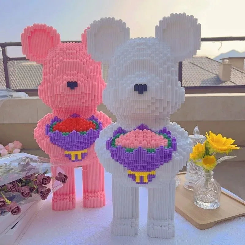 Two bear-shaped sculptures made of interlocking bricks, one pink and one white, holding flower bouquets on a table.