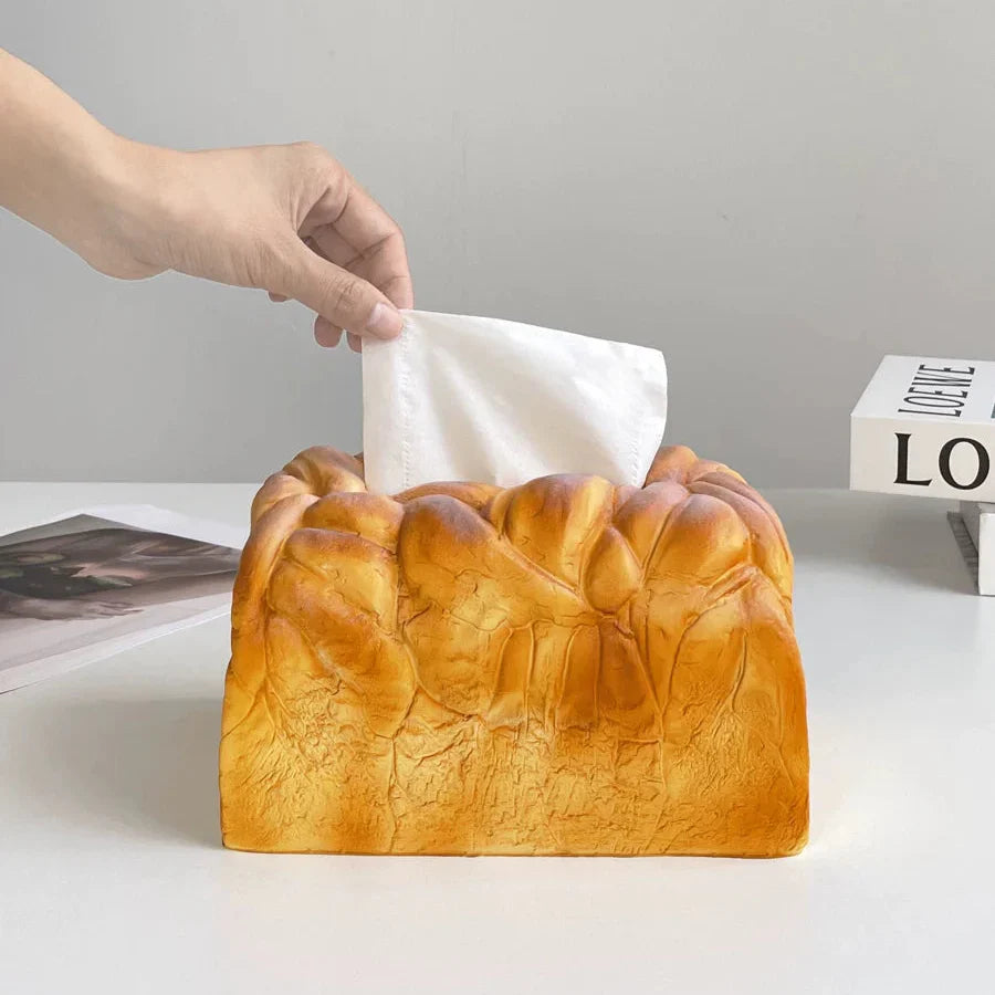 Bread-shaped tissue box with a hand pulling out a tissue against a neutral background