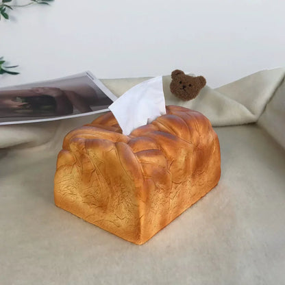 Tissue box shaped like a loaf of bread on a surface with a teddy bear and photo in the background.