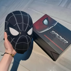Black Spider-Man mask held by a hand next to a Spider-Man box on a light-colored floor.